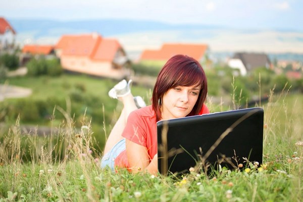 Девушка читает в ноутбуке на пригорке в траве